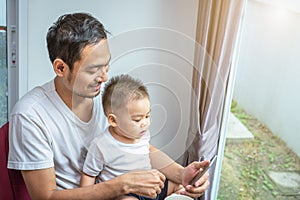 Asian father and son using smart phone together in home background. Technology and People concept. Lifestyles and Happy family