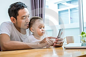 Asian father and son using smart phone together in home background. Technology and People concept. Lifestyles and Happy family th photo