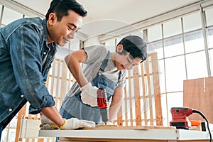 Asian father and son work as a woodworker or carpenter, Father teaches his son to drill holes in a wooden plank carefully together