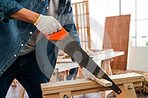 Asian father and son work as a woodworker or carpenter, Father wears safety goggles and saw a wooden plank with hand saw carefully