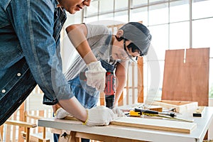 Asian father and son work as a woodworker or carpenters. Close up hands of the father and his son drill holes in a wooden plank