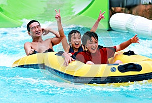 Asian father and sons having fun tubing at a waterpark