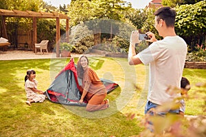 Asian Father Taking Photo On Mobile Phone As  Put Up Tent Family In Garden At Home