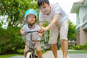 Asian father  teaching his child how to ride a bicycle in a neighborhood garden, fathers interact with their children throughout