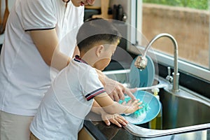 Asian father is teaching his son how to wash dishes, help with housework in the kitchen at home, fathers interact with their photo