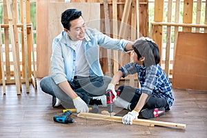 Asian father touch head of his son during drill the timber in home workplace of carpentering with happy emotion. Asian family