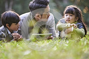 Asian father and two children relaxing outdoors in city park