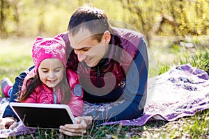 Asian father and two children sitting on grass looking at tablet computer, outdoor in a park