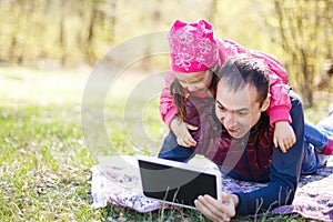 Asian father and two children sitting on grass looking at tablet computer, outdoor in a park