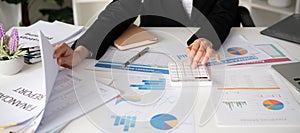 Asian female accountant Use a calculator to calculate business numbers on a white wooden table in the office.