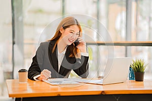 Asian female accountant working on paperwork at office while talking on the phone