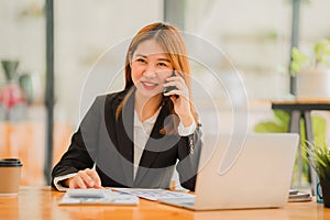 Asian female accountant working on paperwork at office while talking on the phone