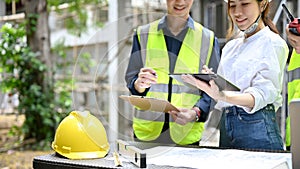 Asian female architect checking some details on clipboard with a team at the construction site