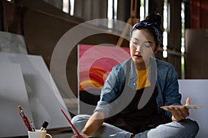 Asian Female Artist Draws create art piece with palette and brush painting at studio.