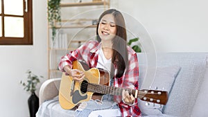 Asian female artist playing the guitar and singing happily in the living room