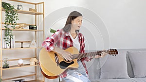 Asian female artist playing the guitar and singing happily in the living room