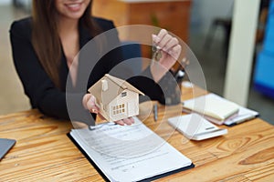 Asian female bank employee handing over a house and keys to a client after signing a contract on paperwork.