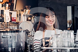 Asian female barista wear jean apron at counter bar with smile face, cafe service concept, owner business start up