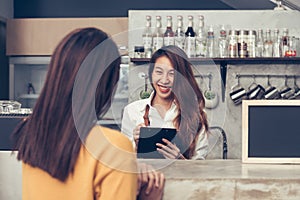 Asian female coffee shop owner taking the order from her client with a warm welcome smile in her small coffe shop.