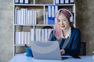 Asian female college student wearing headphones studying online using mobile smartphone app contacting laptop