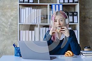 Asian female college student wearing headphones studying online using mobile smartphone app contacting laptop