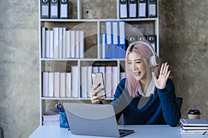 Asian female college student wearing headphones studying online using mobile smartphone app contacting laptop