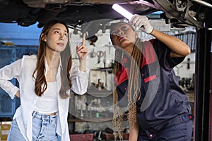 Asian female customer discusses with mechanical worker, check car undercarriage.