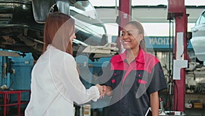 Asian female customer handshakes with automotive worker happy smile at a garage.