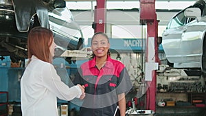 Asian female customer handshakes with automotive worker happy smile at a garage.