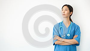 Asian female doctor in blue uniform with crossed arms looks upwards pensive