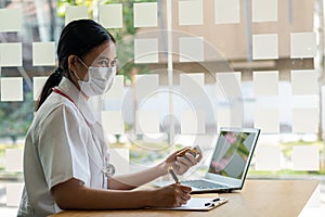 Asian female doctor explains medication procedure to her patient via video call, holding a pill bottle,