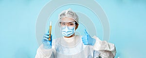 Asian female doctor, lab worker in personal protective equipment, showing thumbs up and test sample tube analise