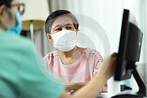 Asian Female Doctor or Nurse in green uniform talking giving advice to Elderly woman patient in pink cloth and looking to computer