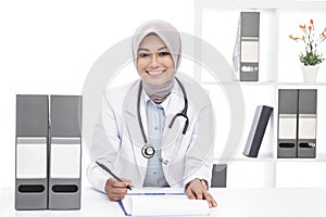 Asian female doctor with stethoscope smiling while writing down