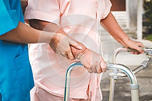 Asian female doctor in surgical gown caring for elderly female patient, helping to walk, doing physiotherapy.