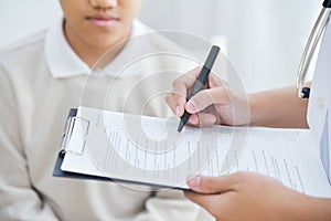 Asian Female Doctor taking note on checklist for a little boy pa