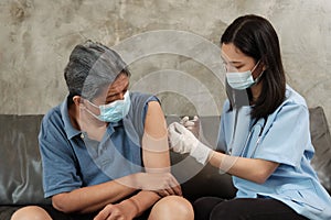 An Asian female doctor is vaccinating an elderly man at home