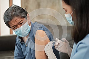An Asian female doctor is vaccinating an elderly man at home