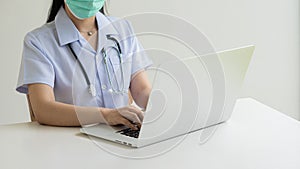 Asian female doctor wearing a mask in a white dress with a stethoscope wrapped around her waist medical student working on laptop