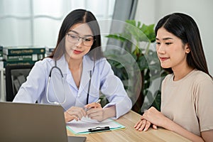 Asian female doctor working on her laptop in consultation with female patient at clinic office Medical worker writing a