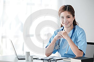 Asian female doctor working on laptop, filling out paperwork, patient medical history, reviewing documents at her