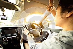 Asian female driver covering face by hand of bright sun,disturbed dazzled by sun light,difficulty in driving,young woman driving