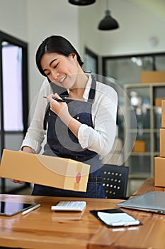 Asian female e-commerce business startup talking on the phone while preparing a package