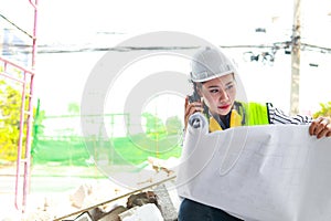 Asian female engineer holding a blueprint at a construction site.