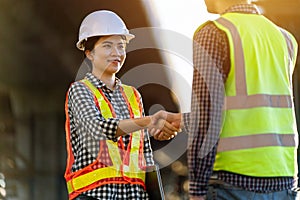 Asian female engineer in protective helmets and wear reflective safety clothing are shaking hands with foreman while working at