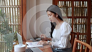 An Asian female entrepreneur working at cafe using a calculator to budget