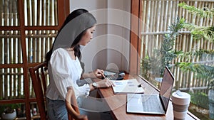 An Asian female entrepreneur working at cafe using a calculator to budget