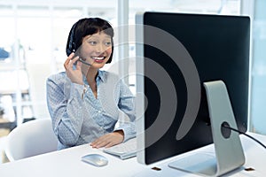 Asian Female executive talking on headset at desk