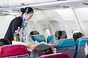 Asian female flight attendant serving food and drink to passengers on airplane. The cabin crew pushing the cart on aisle to serve