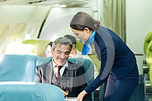 Asian female flight attendant serving food and drink to passengers on airplane. The cabin crew pushing the cart on aisle to serve photo